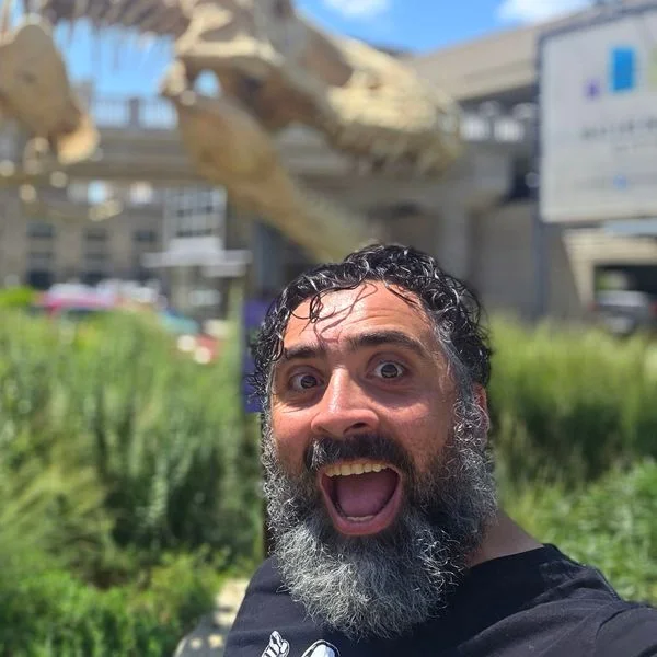 Jeff making a surprised face in front of a dinosaur skeleton sculpture.