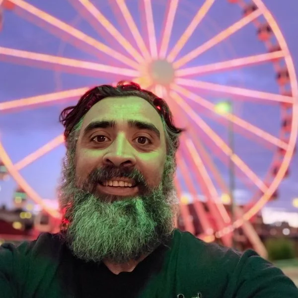 Jeff smiling in front of a Ferris wheel lit up at dusk.