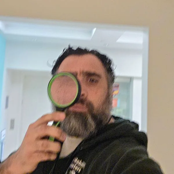 Jeff looking through a magnifying glass, in a KC Mobility hoodie.