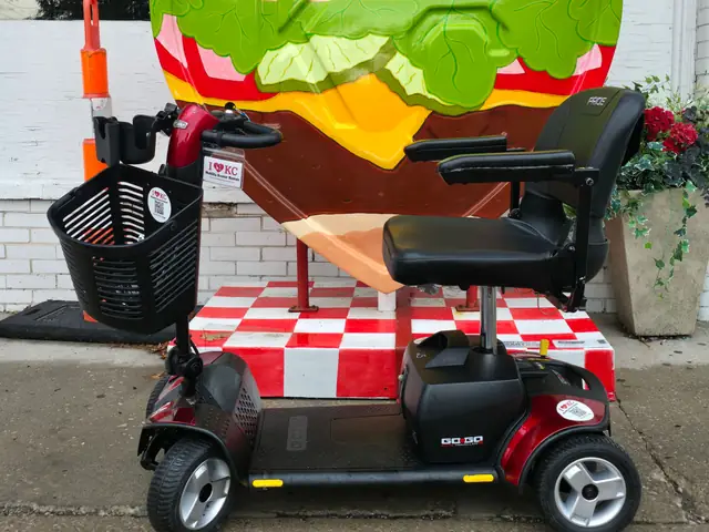 Red Pride Go-Go Sport 4-wheel mobility scooter beside the burger KC heart sculpture at Westport Flea Market, Kansas City
