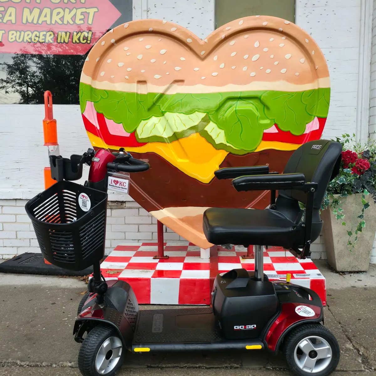 Red Pride Go-Go Sport 4-wheel mobility scooter beside the burger KC heart sculpture at Westport Flea Market, Kansas City