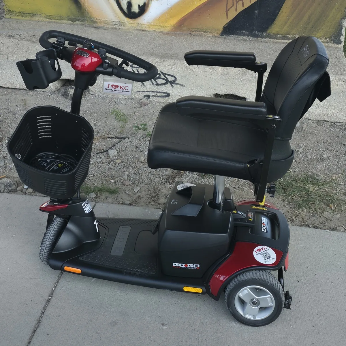 Red Pride Go-Go Elite Traveller 3-wheel mobility scooter on a sidewalk in front of a gold marquee-lights mural in the West Bottoms, Kansas City