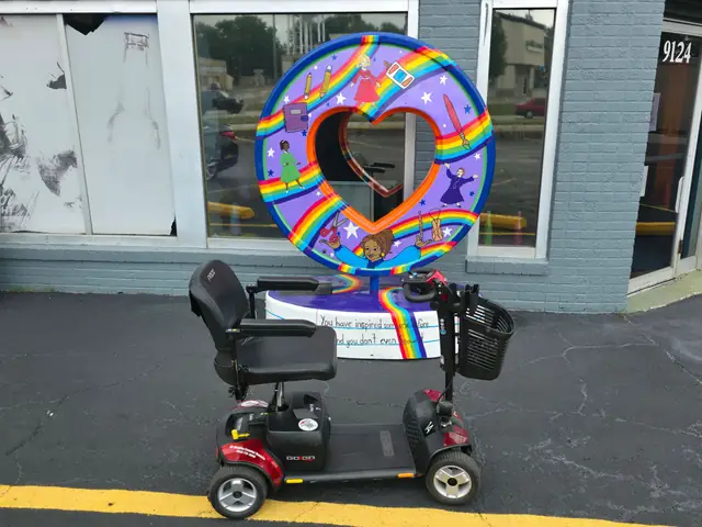 Red Pride Go-Go Traveller 4-wheel mobility scooter in front of a rainbow-painted heart sculpture in the Kansas City area