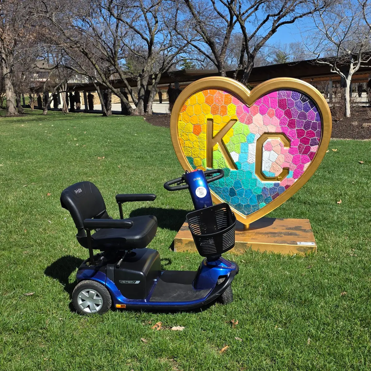 Blue Pride Victory 10 3-wheel mobility scooter beside a rainbow mosaic KC heart sculpture in Kansas City