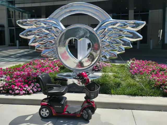 Red Pride Victory 10 4-wheel mobility scooter in front of a silver winged heart sculpture and flower bed in downtown Kansas City