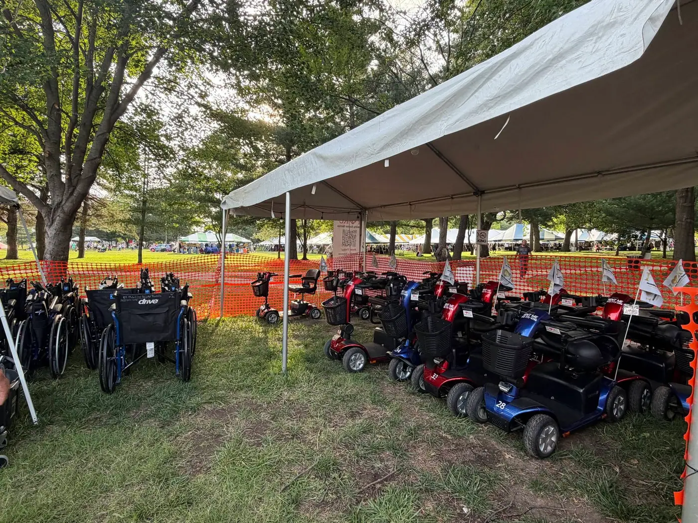 KC Mobility Scooter Rentals' on-site booth at a Kansas City festival — rows of mobility scooters and wheelchairs staged under a tent, ready for guests to rent.