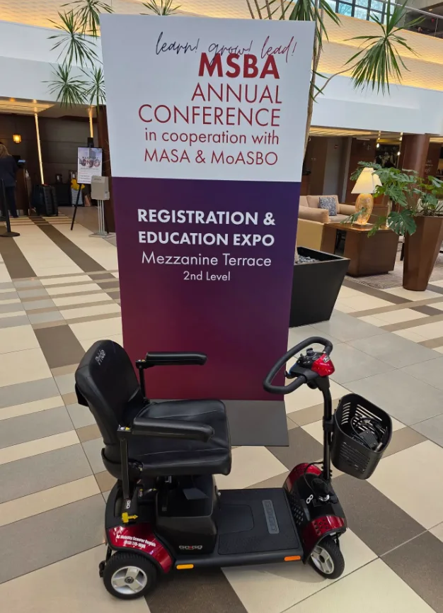Pride Go-Go mobility scooter staged beside a Mezzanine-Terrace Registration & Education Expo banner in a Kansas City conference hotel lobby