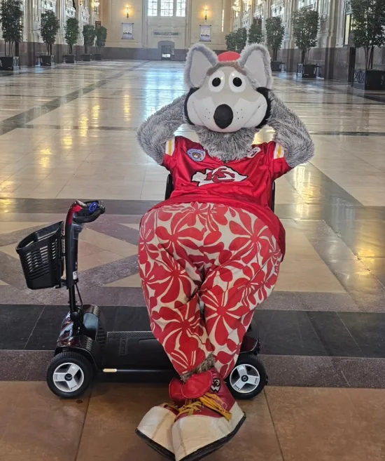 Pride mobility scooter with a costumed game-day mascot in red and gold seated on it, inside Union Station's grand hall in downtown Kansas City