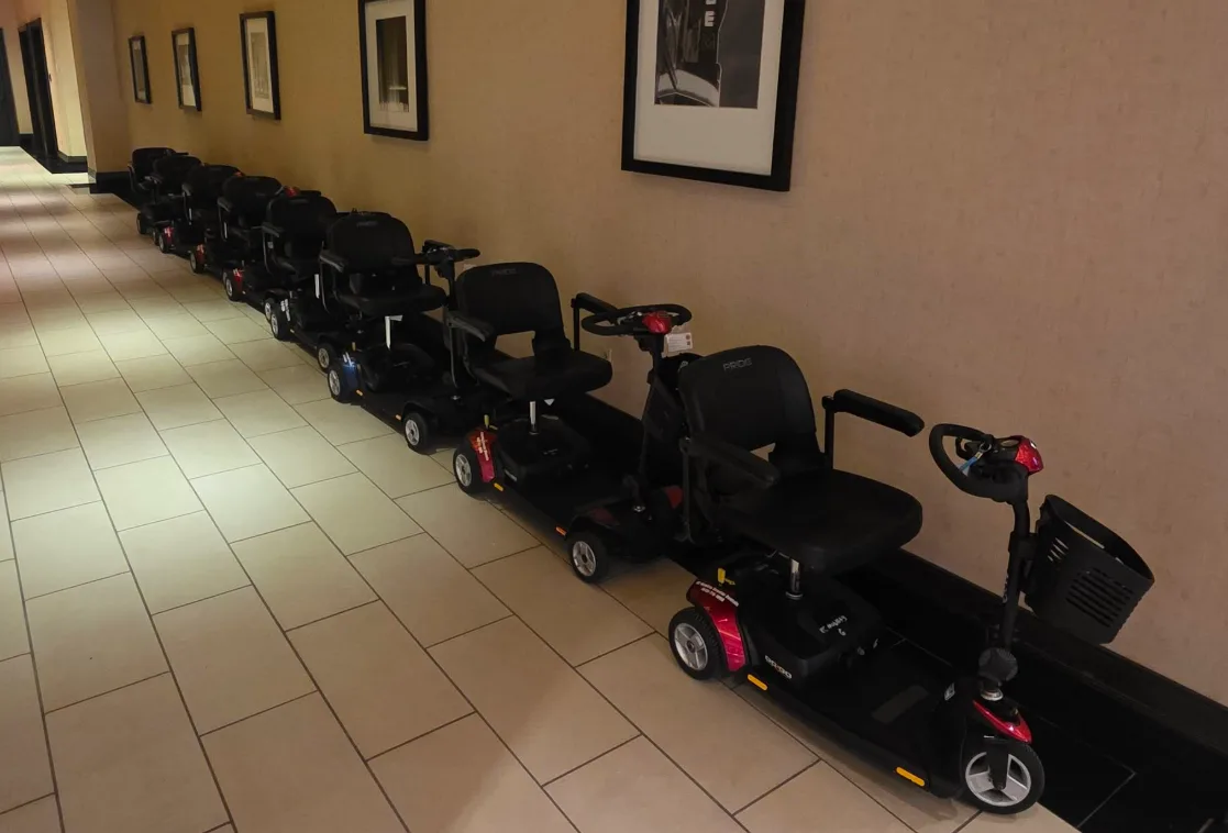 A row of Pride mobility scooters lined up in a hotel hallway, fleet inventory ready for same-day delivery dispatch